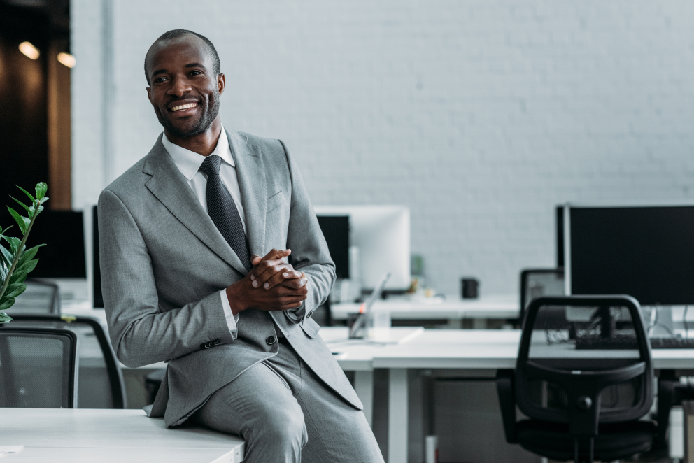 Male financial advisor sitting on desk in office.